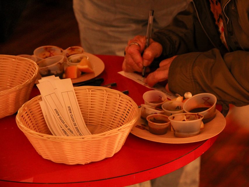 Person writing next to baskets and trays with small food samples and paper slips on a red table.
