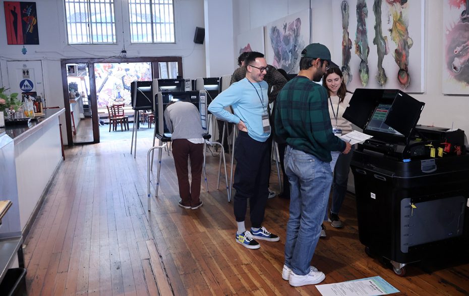 Voters are participating in the election at electronic machines in an indoor polling station adorned with artwork on the walls.