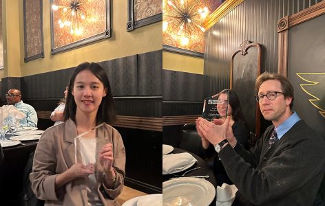 Two people holding triangular glass awards while seated at a dinner table in a restaurant with ornate decorations.