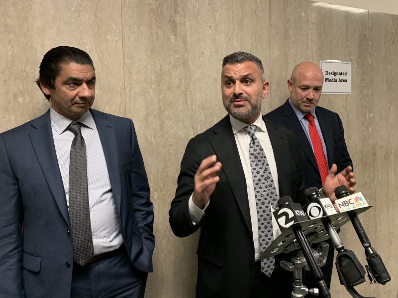 Nima Momeni's attorneys stand near microphones in a designated media area, with one speaking.