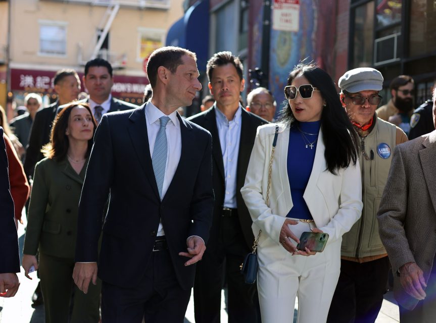 A group of professionally dressed people walk together in an outdoor urban setting.
