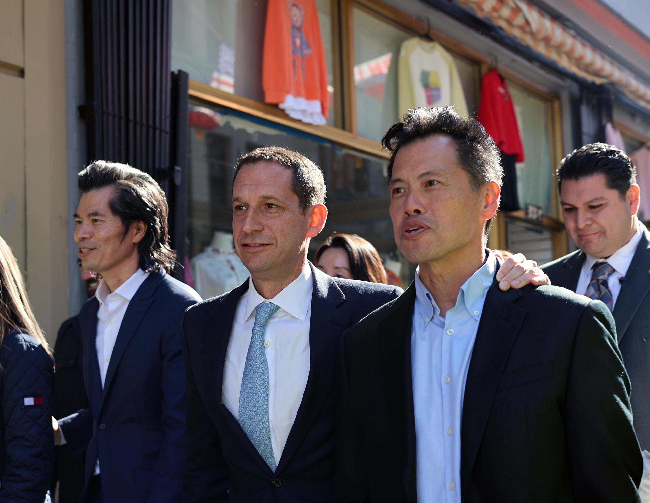 一群身著商務裝的男士在戶外行走，背景可見店面和服飾展示品。