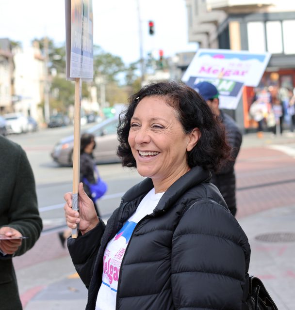 A woman smiles while holding a sign at a street protest.