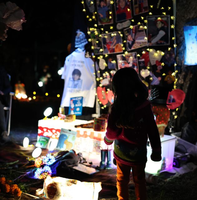 A person looks at a memorial display with photos, lights, and decorations at night.