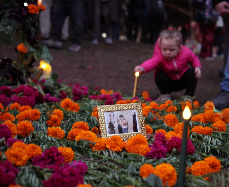 A child places a candle among marigolds and a framed photo on a ground decorated for a memorial.