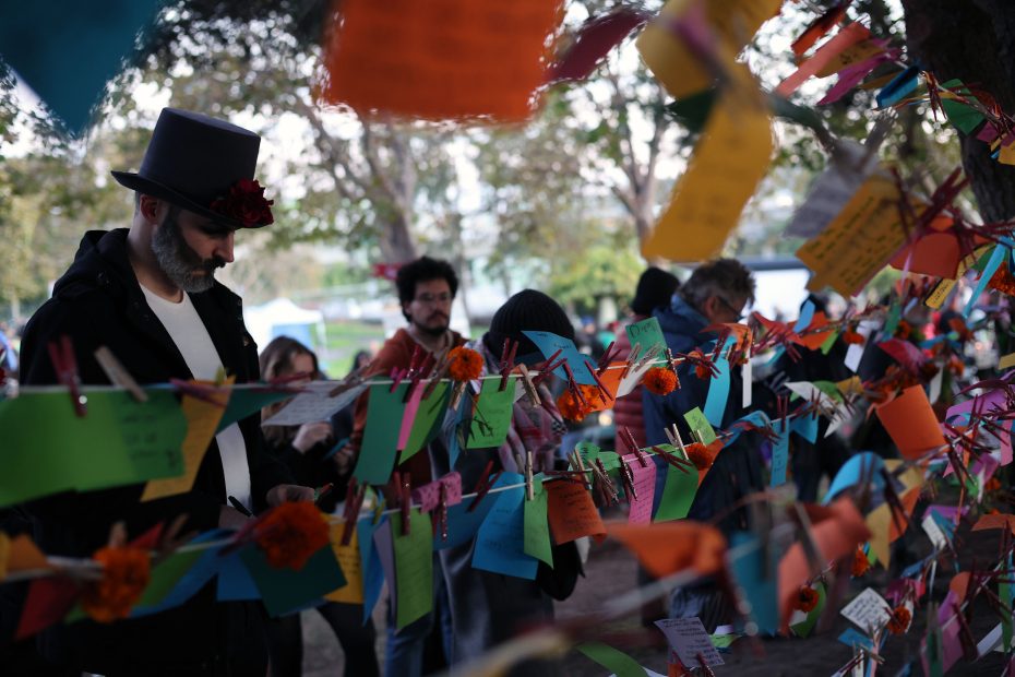 People standing near a tree decorated with colorful paper notes and clothespins during an outdoor event.