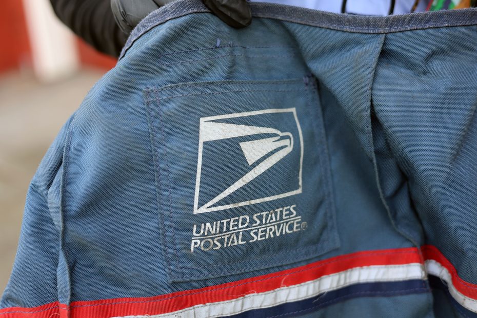 Close-up of a United States Postal Service jacket featuring the USPS logo. A person is holding the jacket.