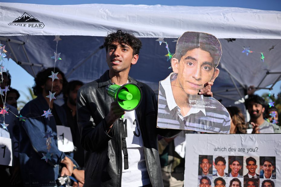 A person with a megaphone holds a photo of another person, surrounded by a group of people under a tent with star decorations.