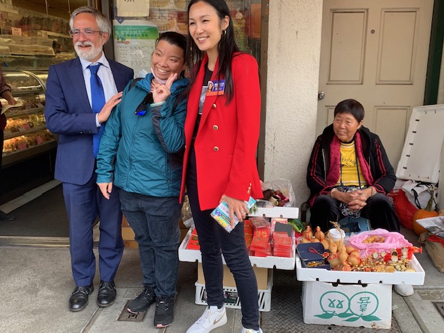 Four people standing outside a shop with a street vendor selling goods in boxes.