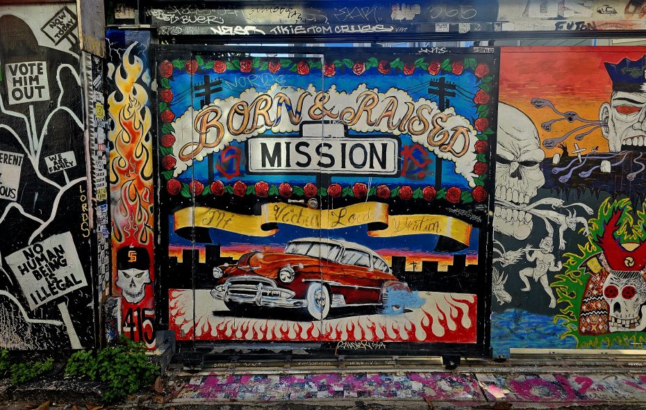 Graffiti mural featuring a classic car with the text "Born & Raised Mission," surrounded by colorful designs, skulls, and various tags.