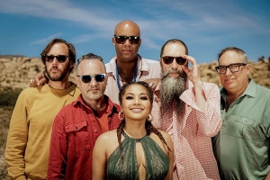 A group of six people standing outdoors on a sunny day, all wearing sunglasses.