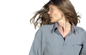 Person with long hair wearing a gray shirt, looking to the side against a plain white background.