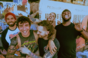 Five people stand together in front of a wall with posters, smiling and making playful gestures.