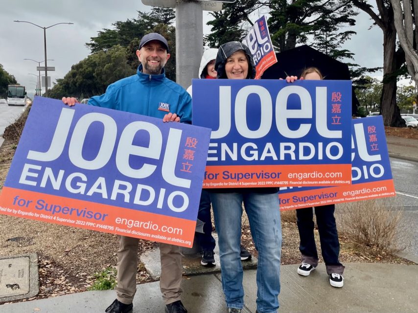 Amidst the drizzle, Joel Engardio and supporters clutch their "Joel Engardio for Supervisor" signs.