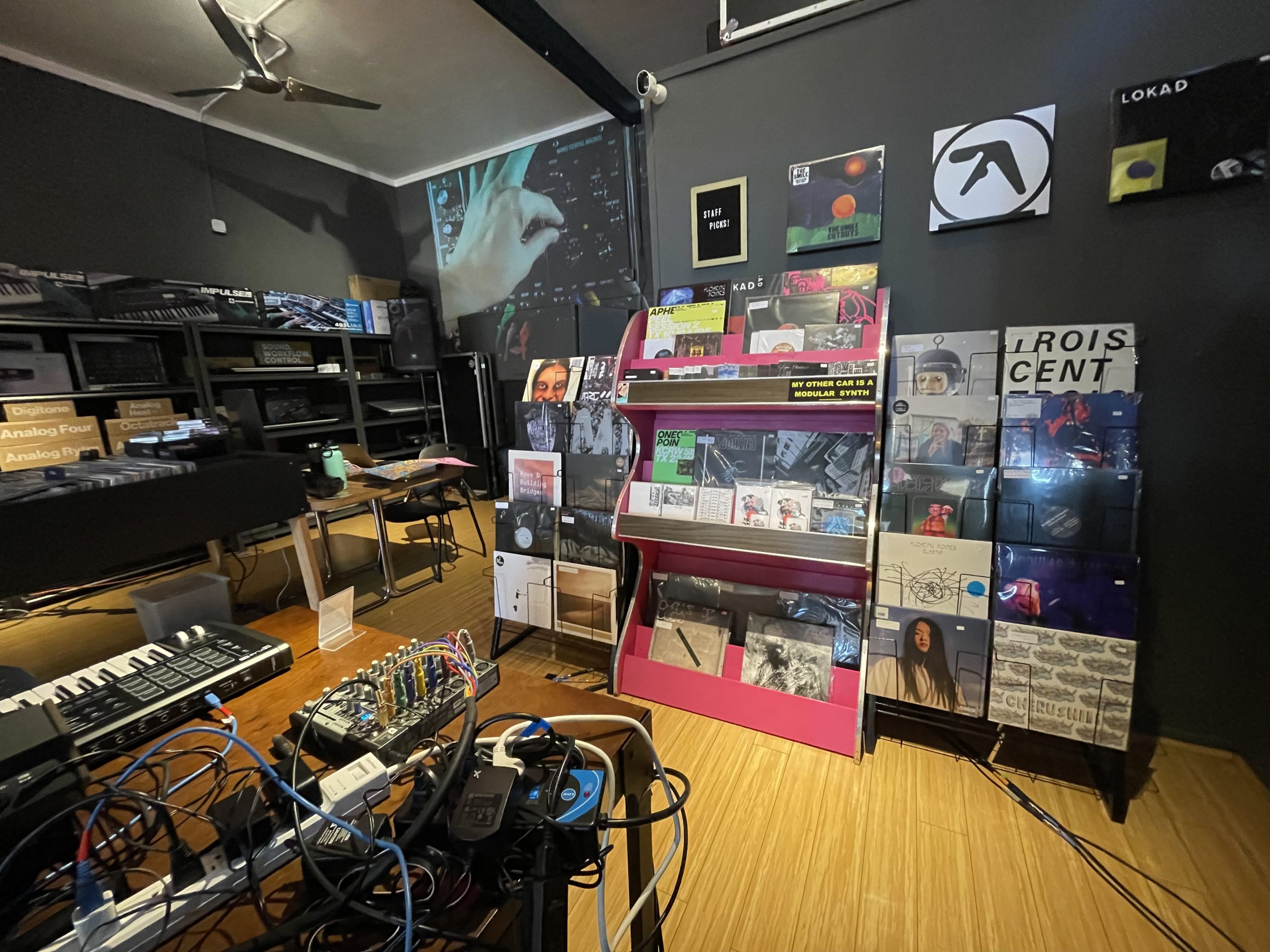 Interior of a music store with shelves displaying vinyl records, a table with electronic equipment, and a projected image on the wall.
