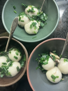 Three bowls of dumplings in broth, each garnished with chopped green onions, with spoons on the side.