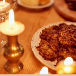 A plate of crispy latkes on a wooden table surrounded by lit candles.