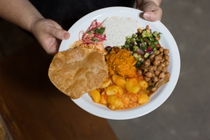 A plate with chickpeas, potatoes, lentils, salad, and a fried bread, held by two hands.