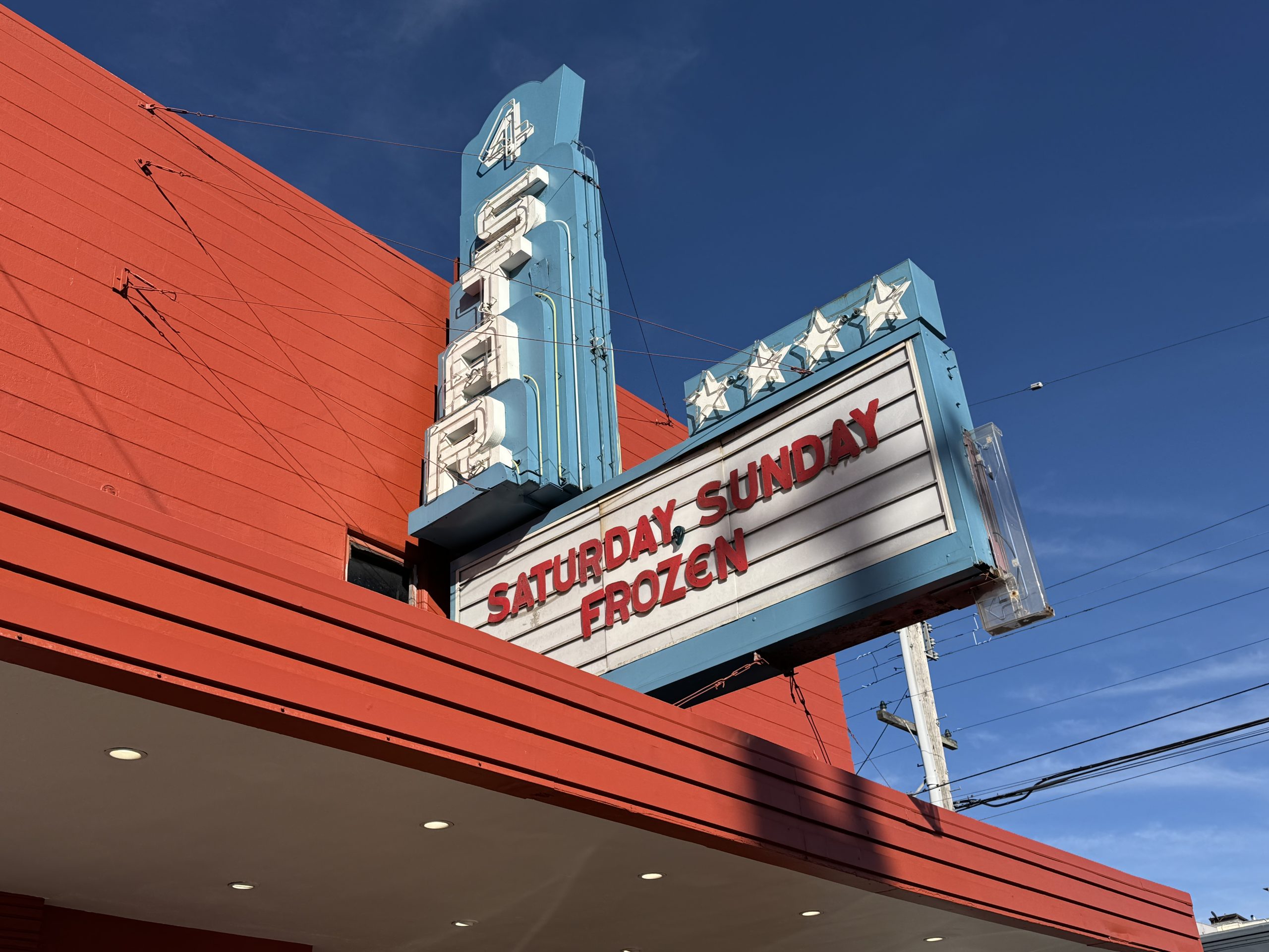 A retro theater with a marquee displaying "Saturday Sunday Frozen" against a clear blue sky.