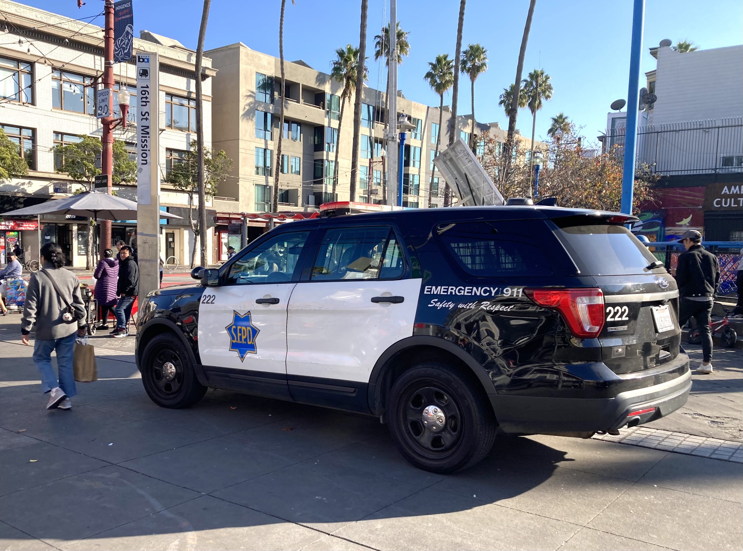 A black and white police SUV marked "SEPD" is parked on a city street near pedestrians and buildings, with palm trees visible in the background.