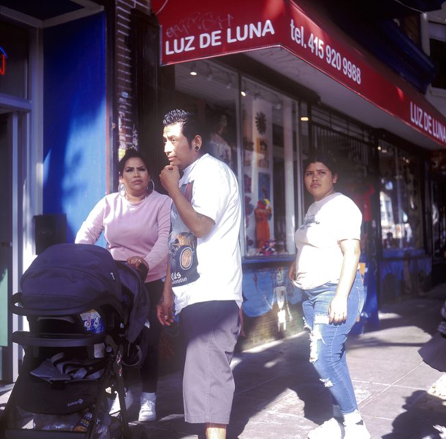 Three people with a stroller stand outside a storefront with a red awning labeled "Luz de Luna" and a phone number.