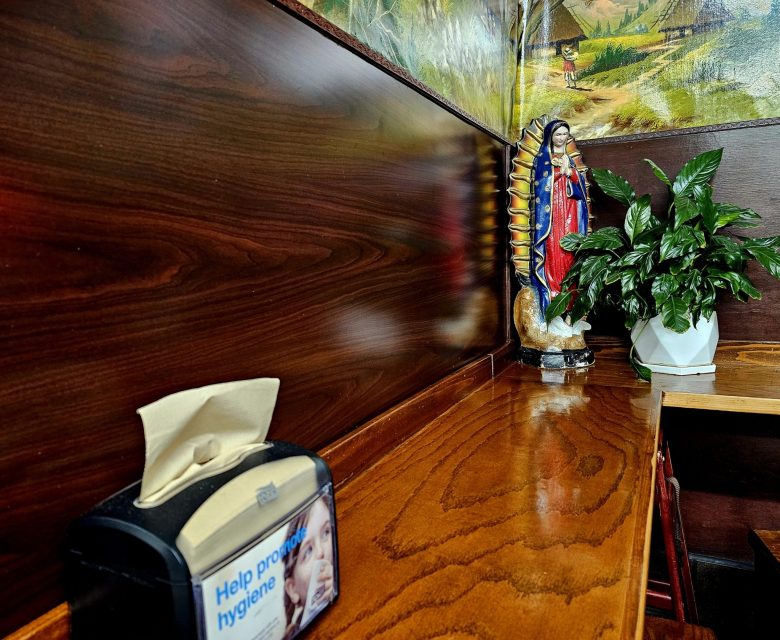 A wooden counter with a tissue dispenser on the left and a Virgin Mary statue next to a potted plant on the right.