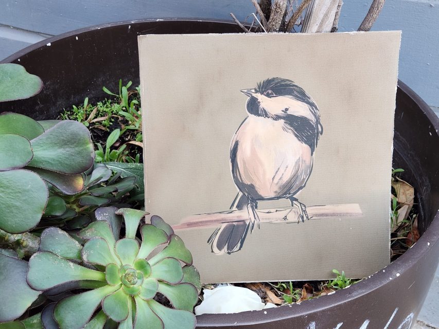 A painted image of a bird on a branch sits inside a large planter with green succulents.