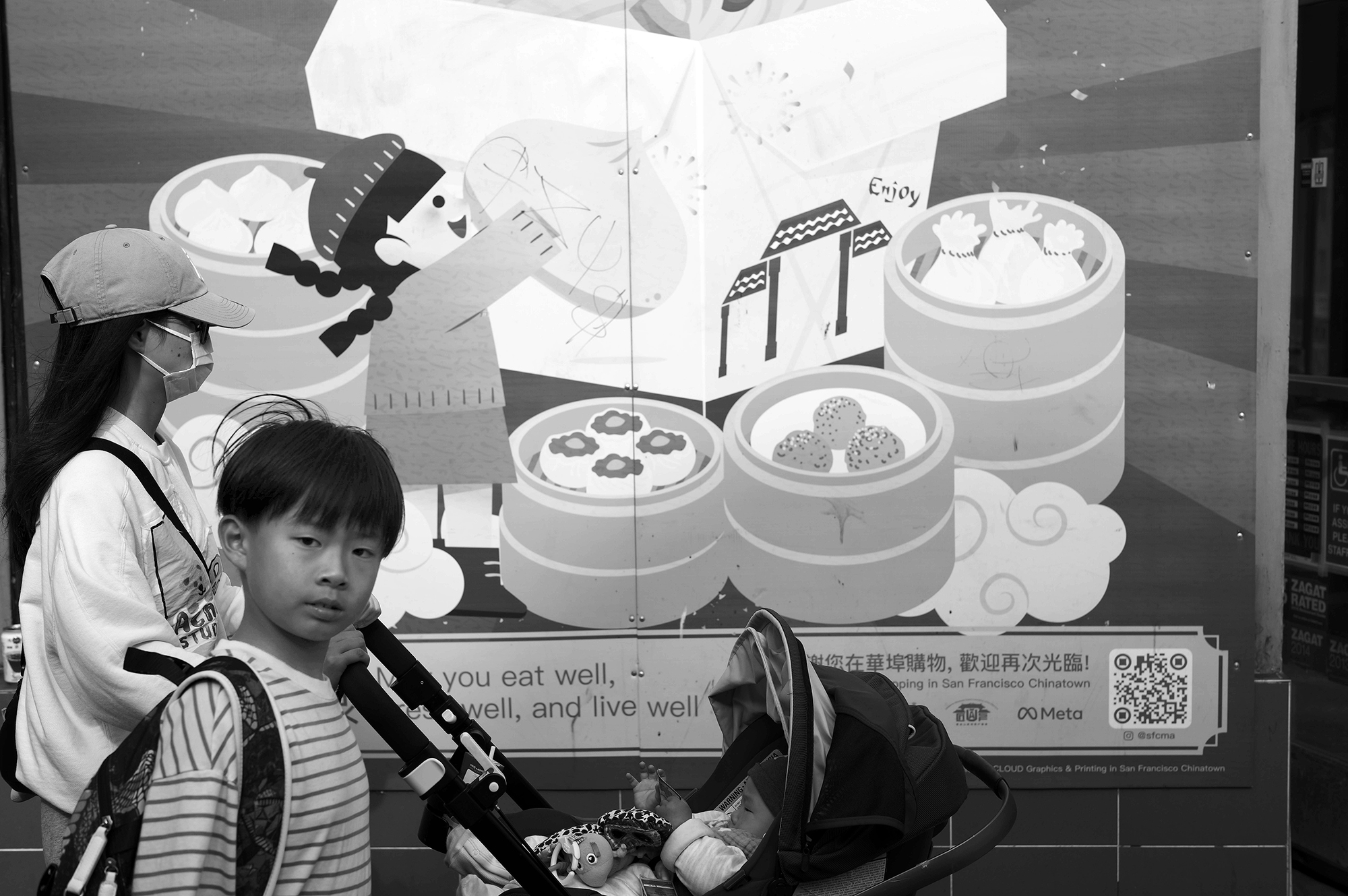 A woman pushing a stroller and a child walk past a large illustrated poster featuring various food items and characters.