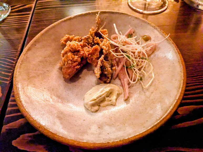A plate with fried chicken pieces, a dollop of mayonnaise, and a small salad with sprouts and red onions.