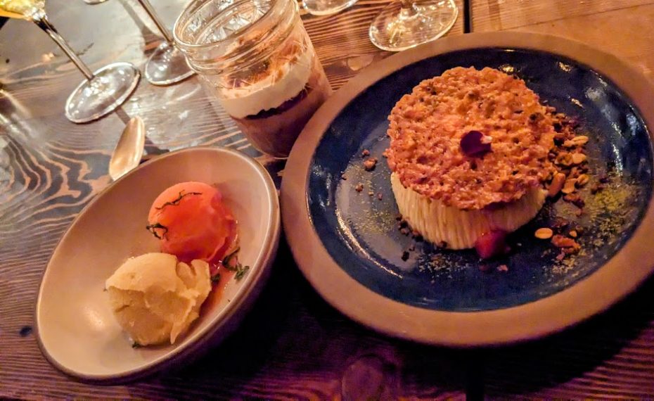 A dessert plate with a tart, a cup with layers of dessert, and a bowl with two scoops of ice cream on a wooden table.