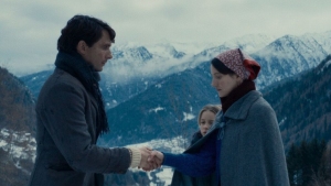 Two people shaking hands in a snowy mountain landscape, with a child looking on in the background.