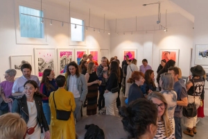 A group of people mingling in an art gallery, viewing framed artworks on the walls.