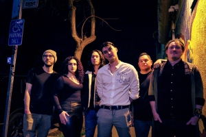 A group of six people stands together outdoors at night, under streetlights.