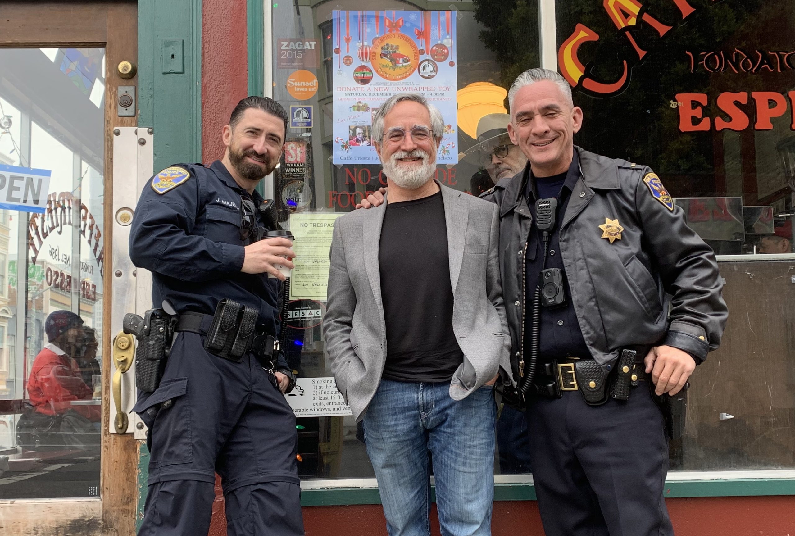Three men, including Peskin in casual attire, pose together outside a café, with two others proudly donning police uniforms.