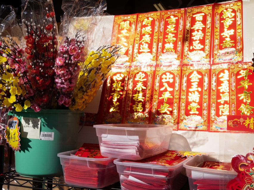 A display of red and gold banners with Chinese characters, a green bucket with artificial flowers, and plastic boxes of red envelopes, likely for a festive occasion.