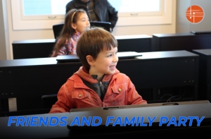 A young child in a red jacket smiles while sitting at a keyboard in a music classroom. Text at the bottom reads "Friends and Family Party.
