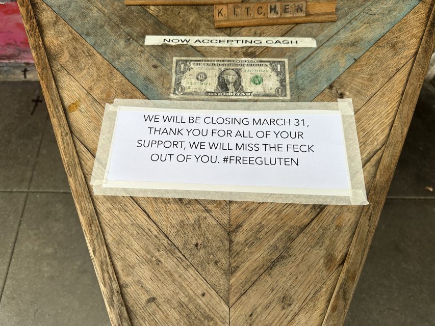 Sign on a wooden table announces a closing date of March 31, expresses gratitude, and includes the hashtag #FREEGLUTEN.