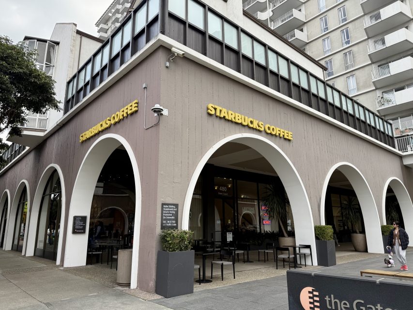 Street view of a Starbucks Coffee location with arched windows and outdoor seating, situated at the base of a multi-story building.