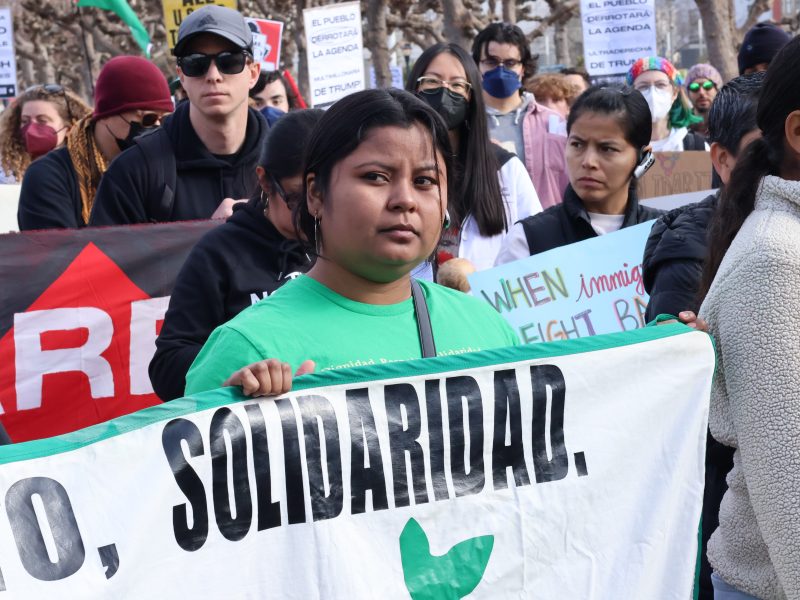 A group of people participating in a protest holds a large white banner with the word "SOLIDARIDAD" on it.