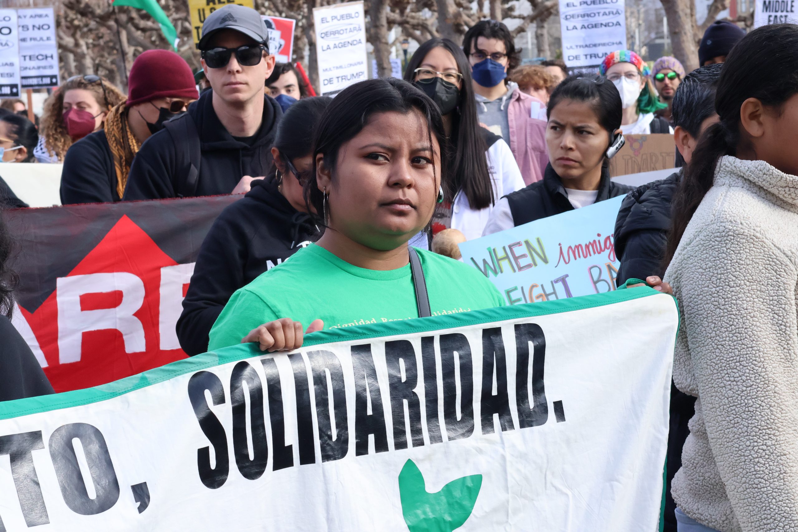 A group of people participating in a protest holds a large white banner with the word "SOLIDARIDAD" on it.