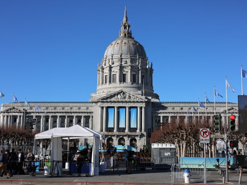 A large domed building with columns, serving as a hub for nonprofit initiatives, is fenced off with security tents and barricades under a clear blue sky.