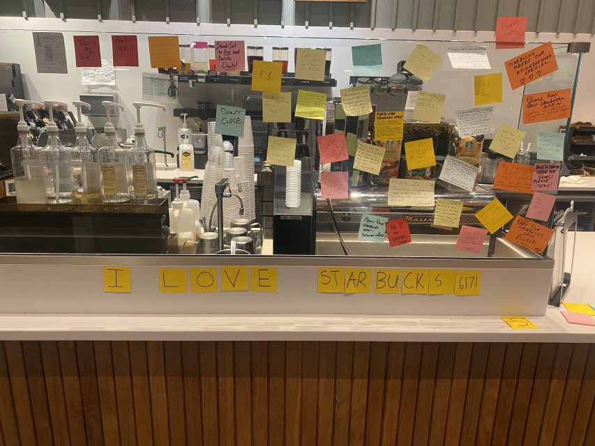 Coffee shop counter with drinks and numerous colorful sticky notes. Sticky notes on the barrier form the sentence: "I love Starbucks!!!!.