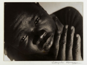 Black and white portrait of a person gazing upward, with one hand partially covering their mouth.