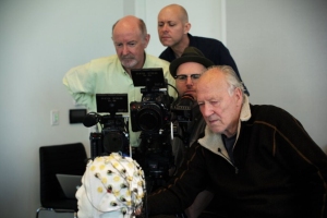 Four men are observing a subject connected to electrodes, with cameras and equipment in a room.