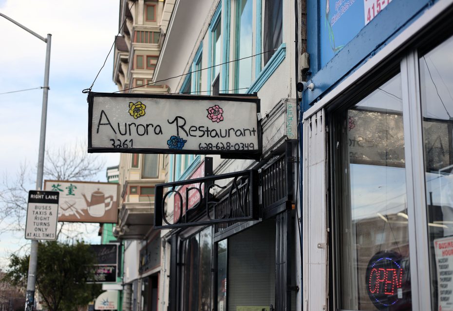 Sign for "Aurora Restaurant" with a phone number hangs above a sidewalk. The restaurant appears open, as indicated by a neon sign in the window.
