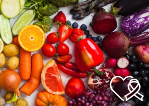 Assorted fruits and vegetables including oranges, tomatoes, grapes, carrots, and more. A heart-shaped ribbon icon is in the lower right corner.