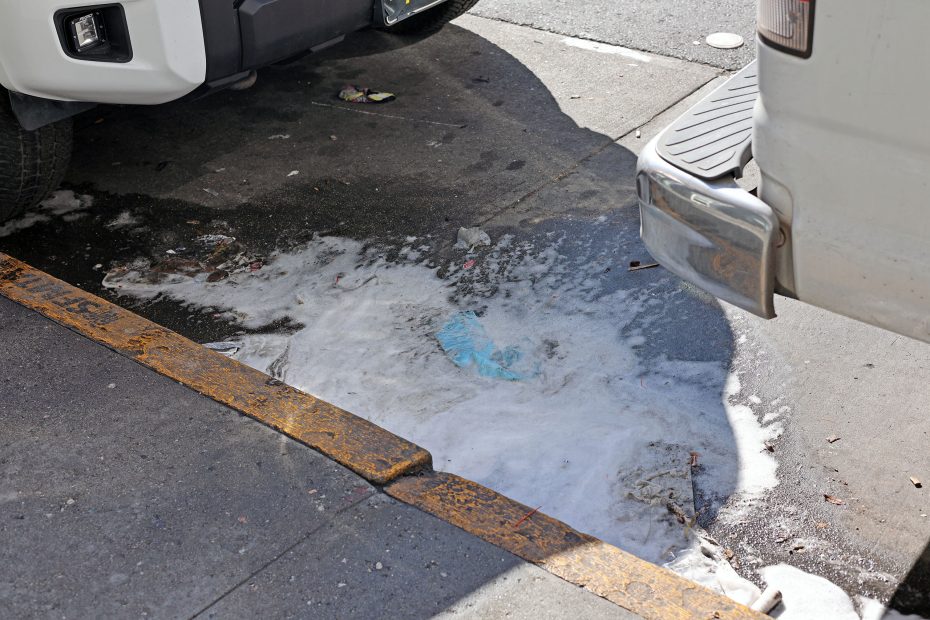 A puddle of white liquid, resembling aftermath debris from a chaotic scene, lay scattered on the pavement between two parked vehicles, hinting at an unsettling incident possibly linked to a shooting.