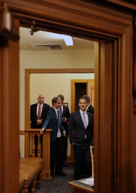 Group of people in formal attire stand in a room, viewed through a wooden doorway.
