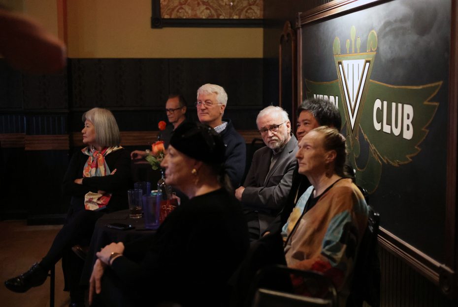 A group of people sitting at a table in a dimly lit room with a sign that reads "Club" in the background.