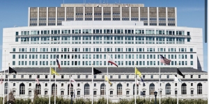 A large, modern building with a series of flags in front against a clear blue sky.
